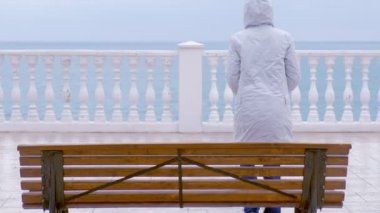 Kadın beyaz ceket ve sahildeki deniz manzaralı güzel terasta hood. Arkadan Görünüm.