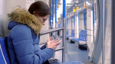 Kadın bir boş metro arabaya biniyor ve bir video onun smartphone üzerinde saatler. Yan görünüm.