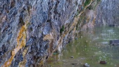 Yağmur damlaları dağ gölünde kayalardan aşağı akar. Yosun ile güzel kayalar mağara, yakın görüş.