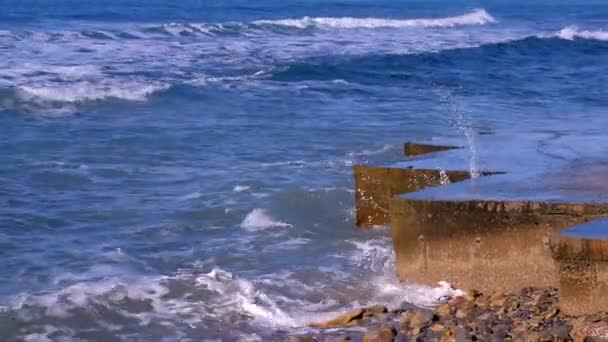 Spatten van water uit de stormachtige golven breken op de golfbreker aan waterkant. Zijaanzicht. — Stockvideo