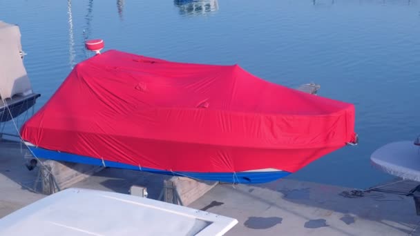 Boot bedekt met rode dekzeil in de zeehaven wordt geparkeerd op de pier. — Stockvideo