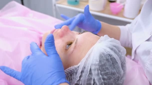 Kosmetolog sätter moisturizer grädde på kvinnans ansikte. Närbild ansikte. — Stockvideo