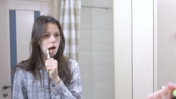 Mujer somnolienta cepillándose los dientes en el baño frente al espejo . — Vídeo de stock