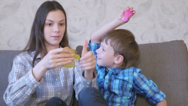 Szczęśliwa mama i syn grają z śluzu, siedząc na kanapie. Rozciąganie szlam. — Wideo stockowe