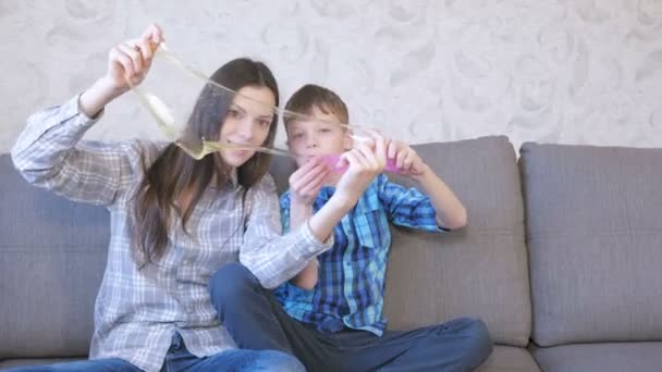 Maman et son fils heureux jouent avec de la boue assise sur le canapé. Étirement de la boue Regardant à travers la boue . — Video