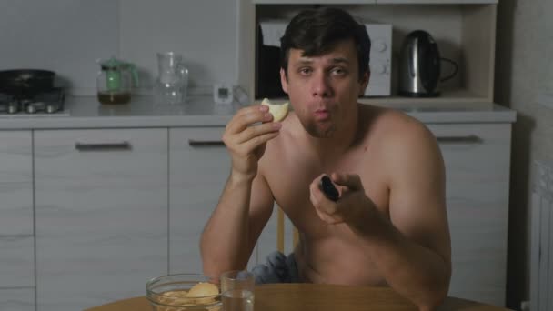 Fiatal férfi, enni a cookie-kat a konyhában éjjel, és nézi a Tv-vel. az álmatlanság és a szorongás. Túlzott élelmiszer. — Stock videók