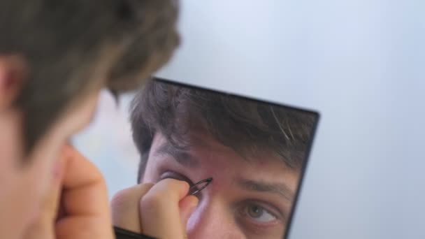 Young man plucks his eyebrows with tweezers in front of the mirror at home. — Stock Video