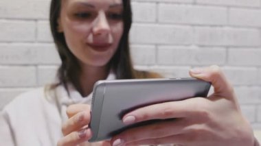 Bir tuğla cep telefonunda kulaklık seri izlerken güzel esmer kadın beyaz duvar arka plan.