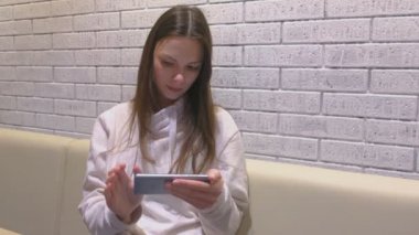 Kadın oturma ve kafede birini bekleyen cep telefonu bir video izliyor.