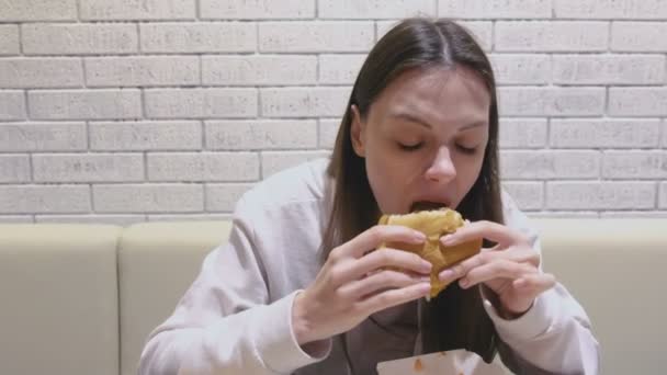 Kvinna äta en hamburgare med välbehag och glädje i café. — Stockvideo