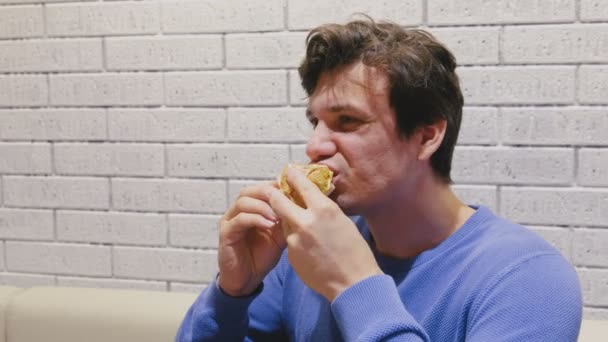 El hombre está comiendo una hamburguesa con gusto y deleite en la cafetería . — Vídeos de Stock