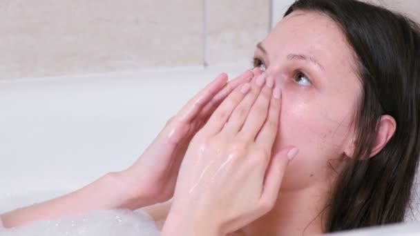 A mulher põe uma bata na cara deitada na casa de banho. Face close-up . — Vídeo de Stock
