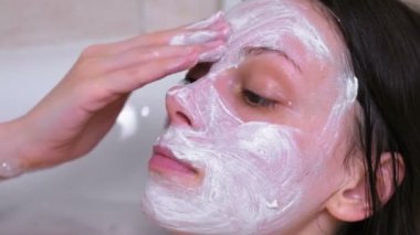 Güzel esmer kadın evde banyoda yalan yüzünde bir maske koyar. Yüz yakın çekim.