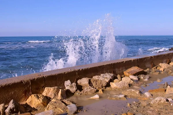 Des éclaboussures d'eau provenant des vagues orageuses se brisant sur le brise-lames sur le front de mer, mer orageuse avec des vagues s'écrasant contre les rochers sous le ciel bleu . — Photo