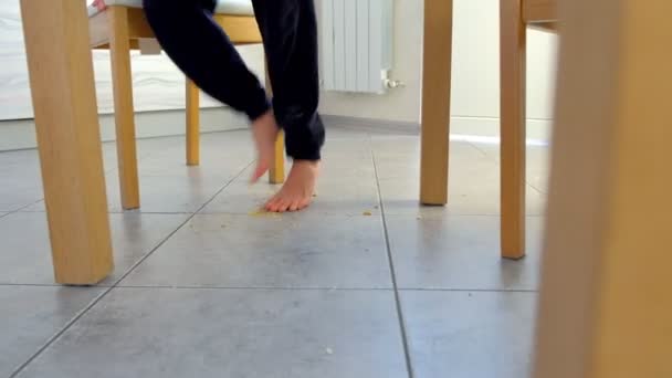 子供がテーブルから立ち上がって、テーブルの下のパンくずに裸足でステップ、彼の足と葉を振ります。フィートクローズアップ. — ストック動画