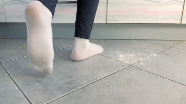 Frau kocht auf dem schmutzigen Fußboden in der Küche. Essensreste und Krümel auf dem Küchenboden. Beine in weißen Socken in Großaufnahme. — Stockvideo