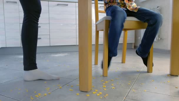 Anya szidás fia szétszórt élelmiszerek a konyhában padlón, és teszi őt megtisztítása. Fiú megtisztítása kukoricapehely le a padlóról. — Stock videók