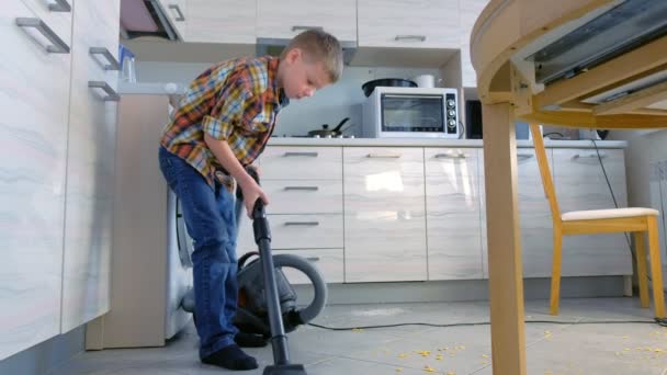 少年は台所の床を掃除機します。彼の灰色のタイル上に散在コーンフレーク体裁が整います。横から見た図. — ストック動画