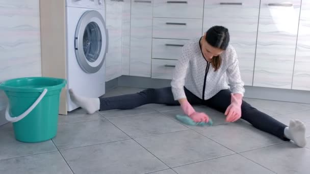 Mujer cansada en guantes de goma rosa lava y frota duro la mancha en el suelo de la cocina con un paño. Azulejos grises en el suelo . — Vídeo de stock