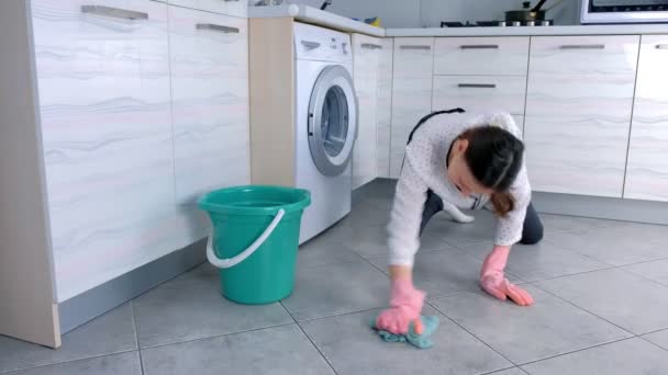 Mujer cansada con guantes de goma rosa lava el suelo de la cocina con un paño. Azulejos grises en el suelo . — Vídeo de stock