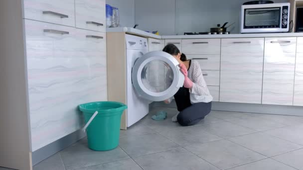 Woman in Pink gumi kesztyű mossa mosógép ruhával, ül a padlón. Oldalnézet. — Stock videók