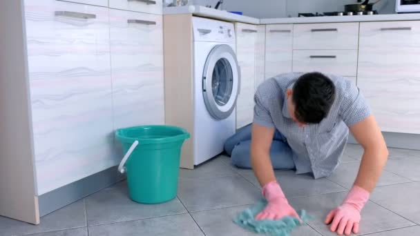 Homem cansado infeliz em luvas de borracha lava o chão na cozinha e olha para a câmera no final . — Vídeo de Stock