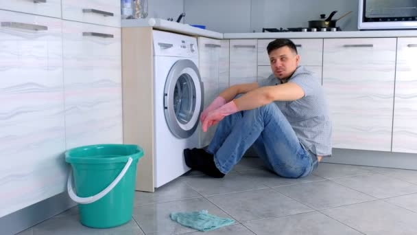 Homem de luvas de borracha tem um descanso de limpar e falar com alguém sentado no chão da cozinha . — Vídeo de Stock