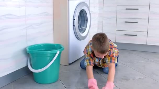 Niño con guantes de goma lava el suelo en la cocina jugando con tela. Funciones domésticas para niños . — Vídeo de stock