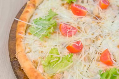 Tavuk ve peynir, domates ve marul üzerine ahşap tahta üzerinde pizza.