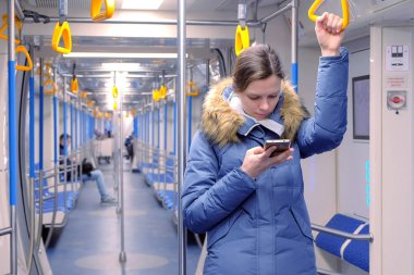 Kadın bir boş metro araba ve onun smartphone üzerinde tarama rides. Standları ve Küpeşte tutar.