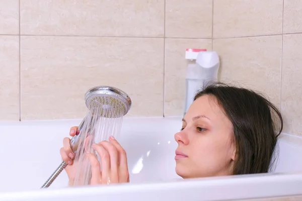 Vrouw is het nemen van een bad. Ze giet haar lichaam water uit de douche. Close-up gezicht. — Stockfoto