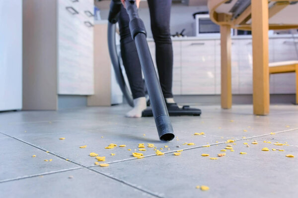 Woman is vacuuming the kitchen floor without brush, only pipe. Legs close-up.