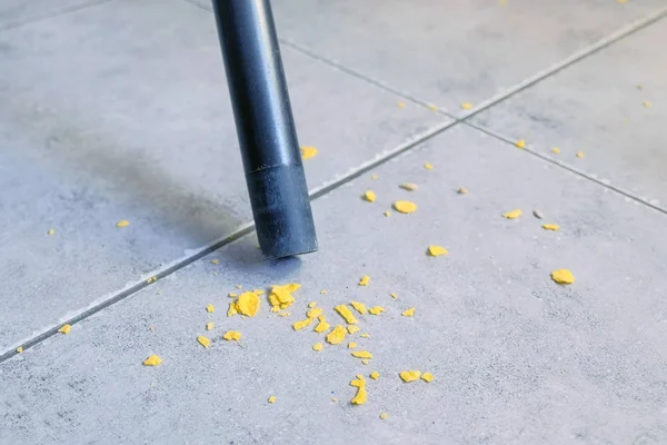 Vacuuming the kitchen floor with grey tile without brush, only pipe of vacuum cleaner. Close-up view.