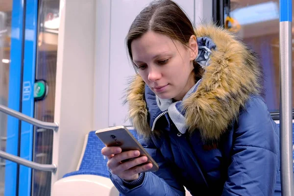 Porträt einer müden Frau, die in einem leeren U-Bahn-Wagen fährt und auf ihrem Smartphone surft. Frontansicht. — Stockfoto