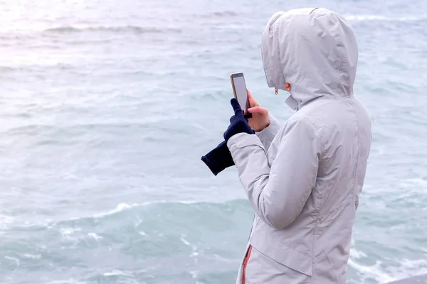 Femme dans une veste blanche prend un téléphone portable grosses vagues de tempête. Vue arrière . — Photo
