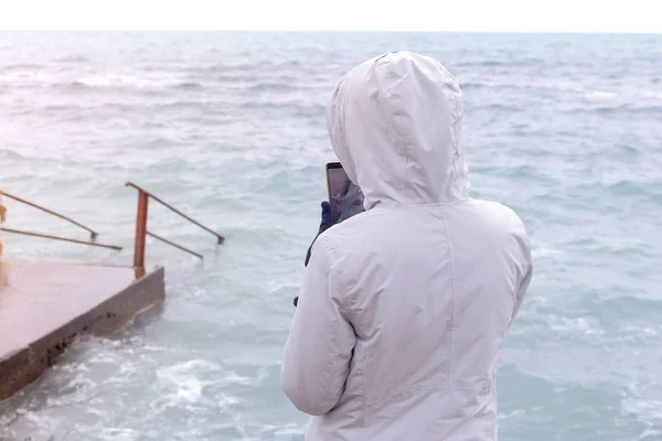 Femme dans une veste blanche prend un téléphone portable grosses vagues de tempête. Vue arrière . — Photo