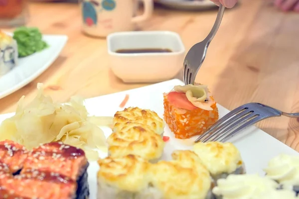 La mujer pone wasabi y jengibre en los rollos y se los come con un tenedor. Primer plano de las manos . —  Fotos de Stock