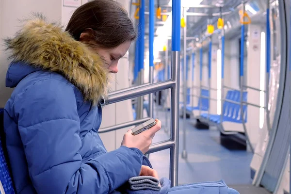 La mujer va en un vagón de metro vacío y ve un video en su teléfono inteligente. Vista lateral . — Foto de Stock