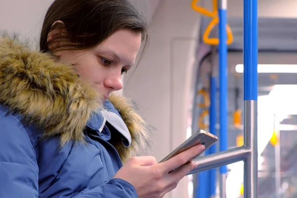Портрет уставшей женщины идет в пустой вагон метро и просматривает свой смартфон. Вид сбоку . — стоковое фото
