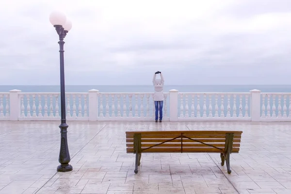 Femme en veste blanche et capuche sur belle terrasse avec vue mer sur le front de mer. Vue arrière . — Photo