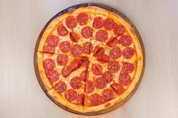 Salami-Pizza auf Holzbrett auf dem Tisch in Scheiben schneiden. Nahaufnahme von oben. — Stockfoto