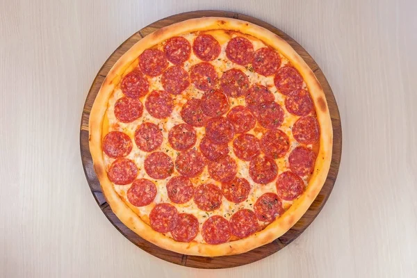 Salami-Pizza auf Holzbrett auf dem Tisch in Scheiben schneiden. Nahaufnahme von oben. — Stockfoto