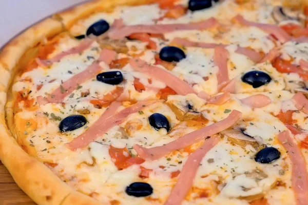 Pizza mit Schinken und Käse auf Holzbrett auf dem Tisch. Nahaufnahme. Seitenansicht. — Stockfoto