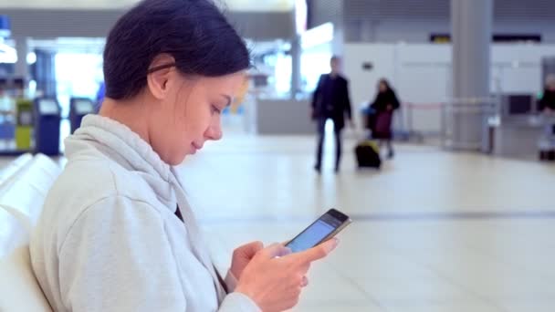 Donna in aeroporto con un telefono cellulare in mano messaggiare messaggio e in attesa del suo volo, vista laterale . — Video Stock