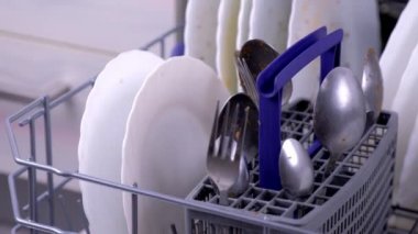 Mutfakta kirli beyaz yemekler ve çatal-bıçak takımı ile bulaşık makinesi sepeti.