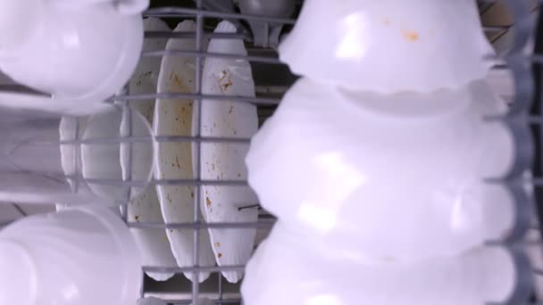 Main Mans met une vaisselle sale blanche dans le lave-vaisselle et pousse les paniers avec des ustensiles de cuisine. — Video