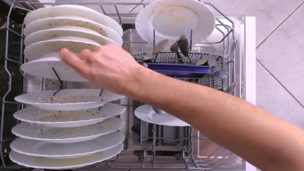 Mans mão coloca pratos sujos brancos e colher na máquina de lavar louça e empurra a cesta com utensílios de cozinha . — Vídeo de Stock