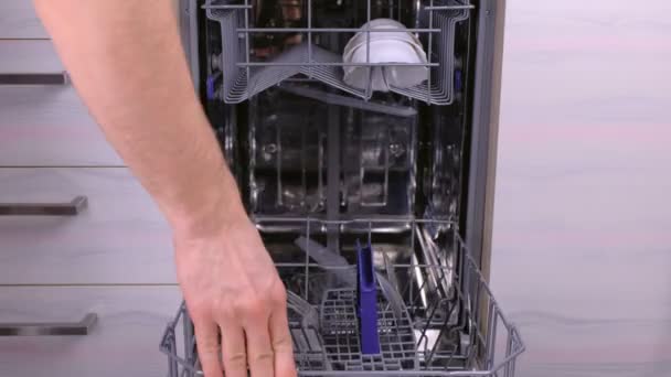 Mans mão está colocando um branco pratos sujos e talheres na cesta da máquina de lavar louça . — Vídeo de Stock