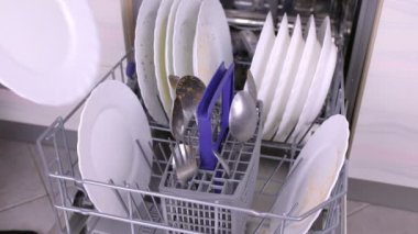 Mans el bulaşık makinesine beyaz kirli bir tabak ve kaşık koyarak ve mutfakta çalışıyor.