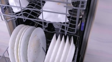 Mutfakta bulaşık makinesi sepetlerinde kirli beyaz tabaklar.